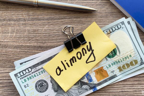 A stack of money held together with a binder clip and a sticky note that says "alimony".