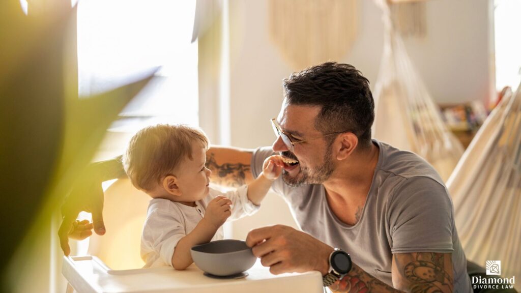 A father feeding and playing with his child at the kitchen table.