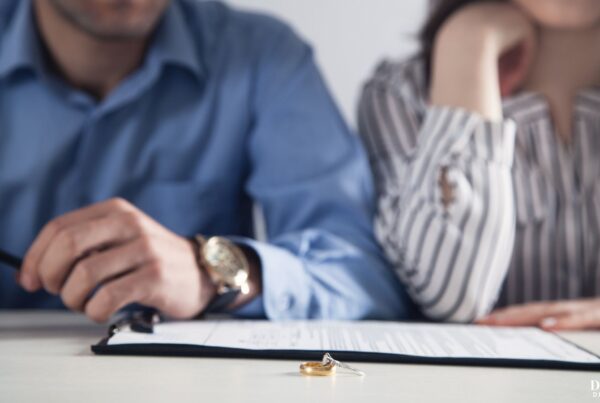 A man and woman signing divorce papers with their wedding rings sitting on the table in the foreground.