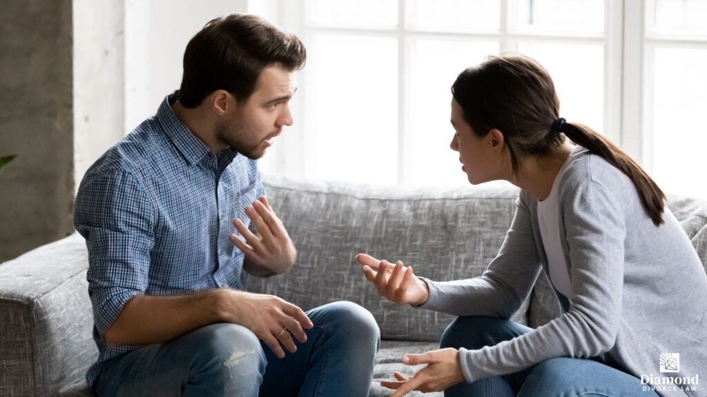 A husband and wife sitting on a couch arguing.