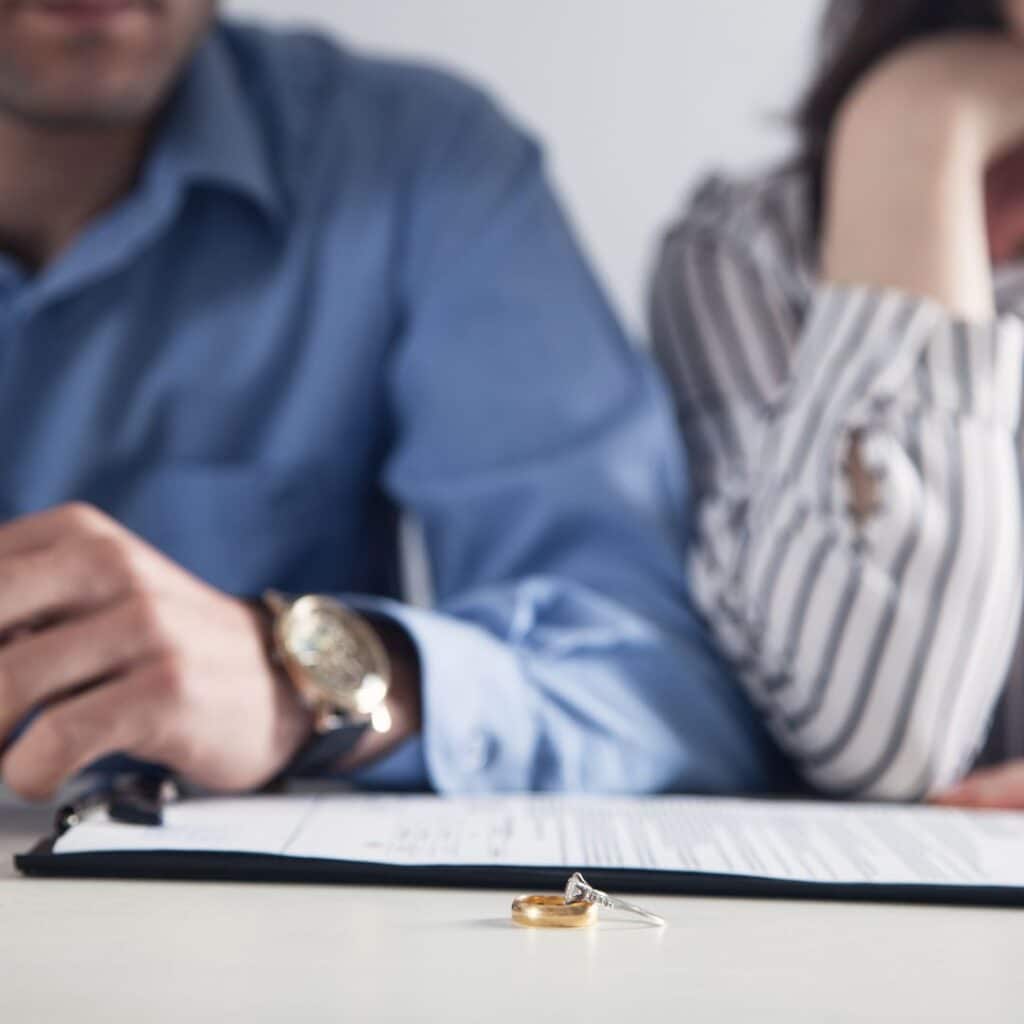 A man and woman signing divorce documents with their wedding rings in the foreground.