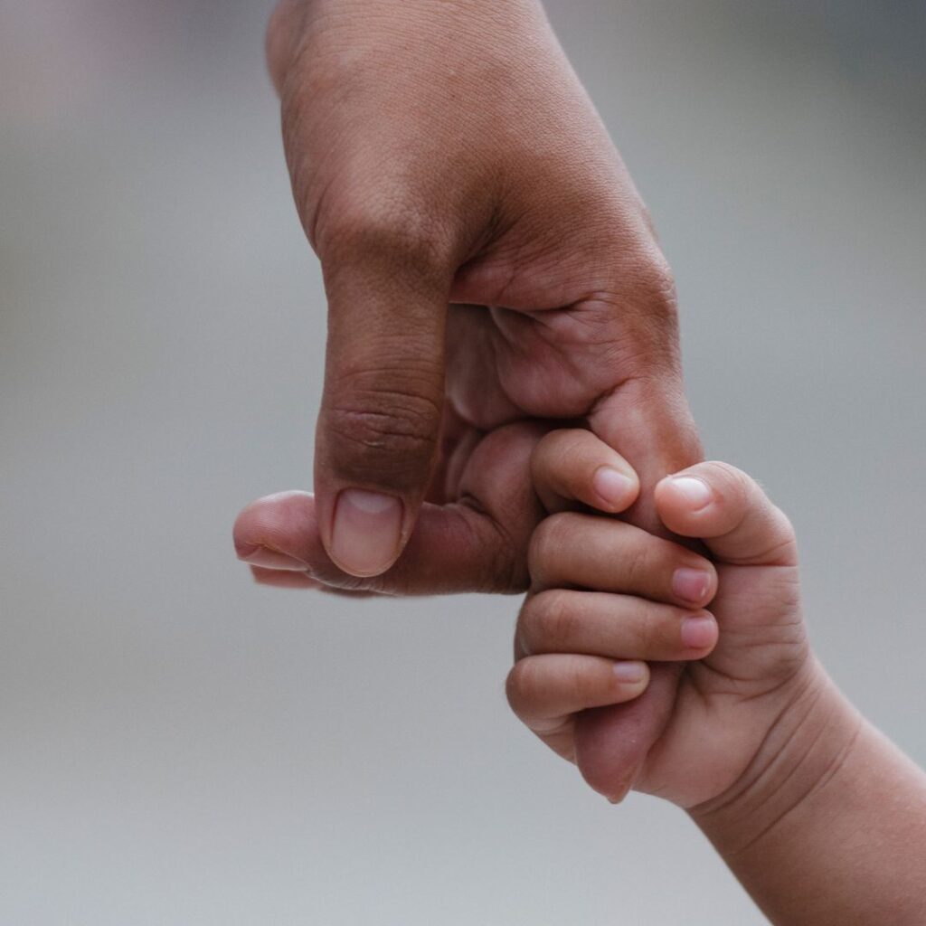 The hand of a small child holding onto their father's finger.