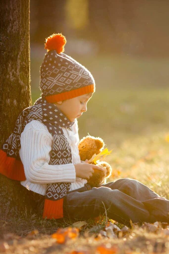 A little boy in a sweater, scarf, and stocking cap sitting beneath a tree playing.