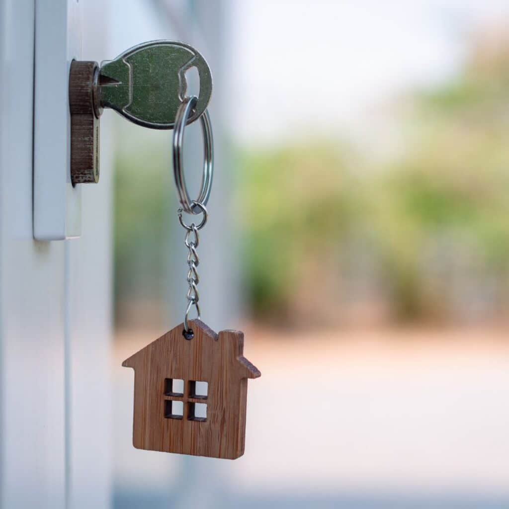 A keychain with a wooden house hanging from a home's front door.