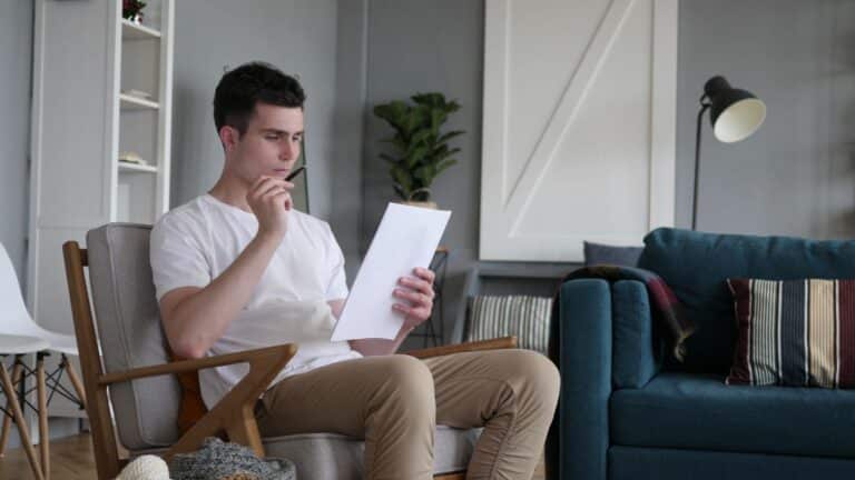 A man sitting in his living room, looking through paperwork.