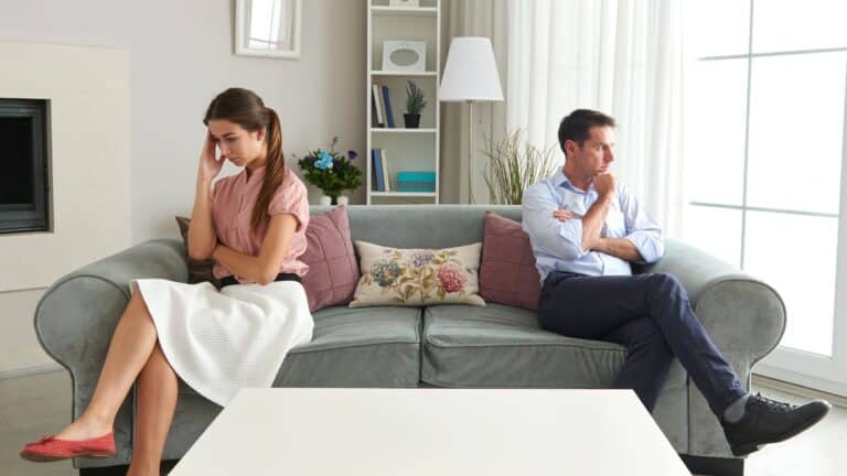 A frustrated couple sitting on either end of their couch, looking in opposite directions.